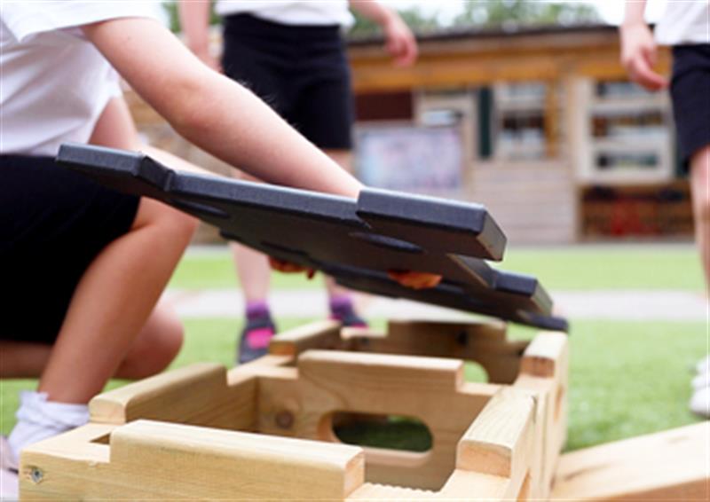 Child slotting together a black lid into a wooden Play Builder block